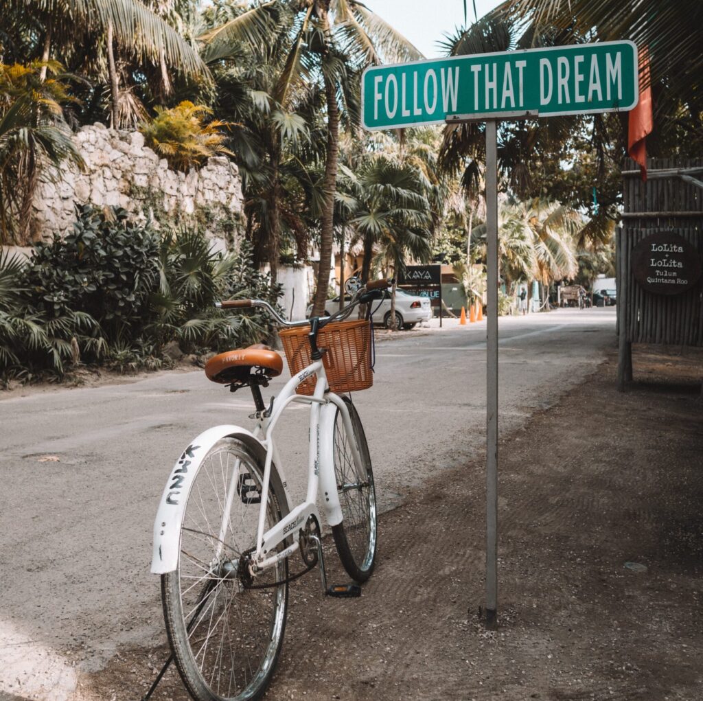 A street sign that reads follow that dream next to a bicycle 