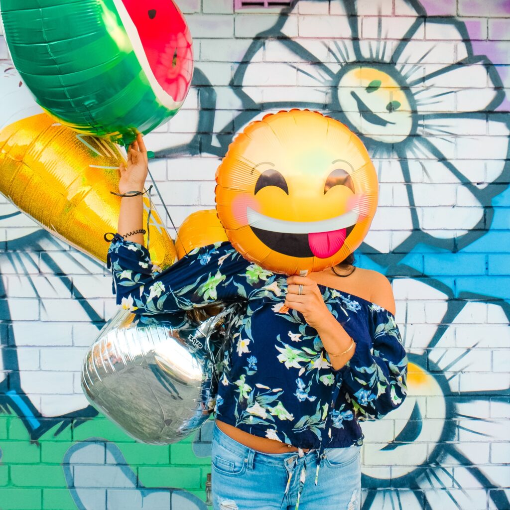 a woman holding a smiley balloon over her face